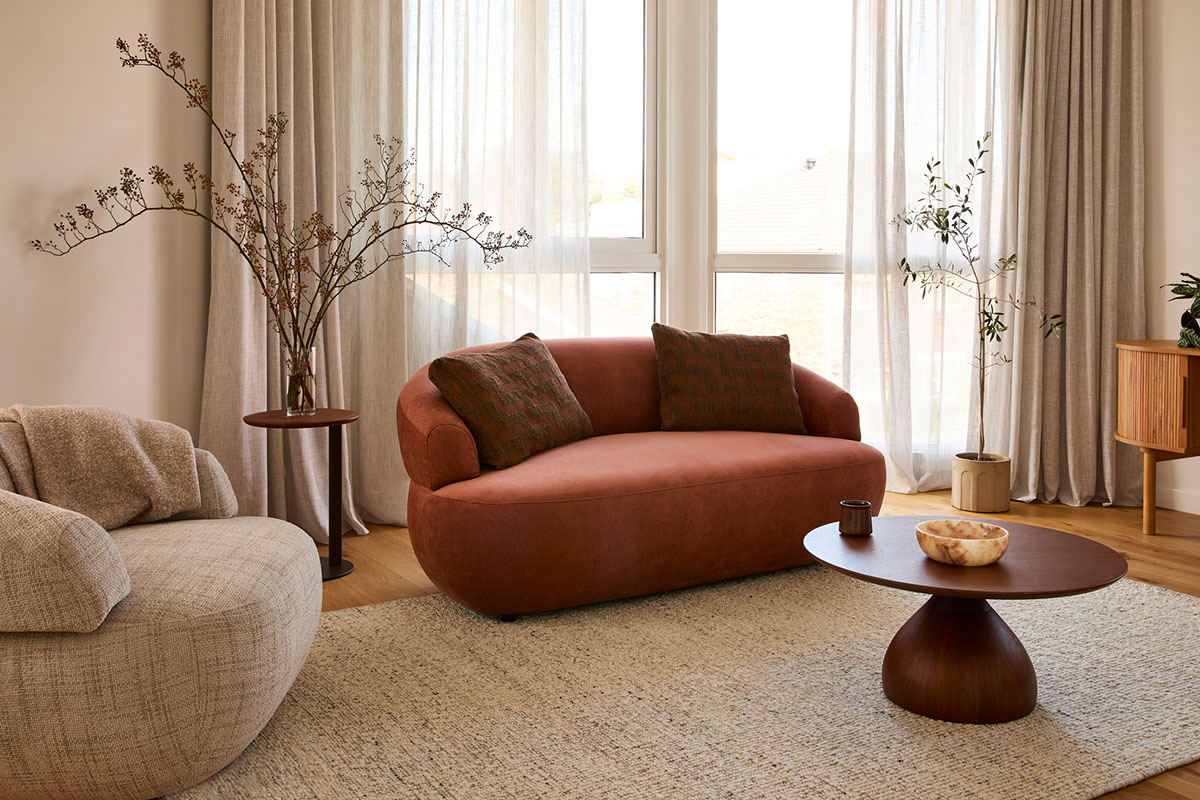 Aura 2 Seater Sofa and Swivel Chair. A curved loveseat in a warm rust toned fabric styled in a contemporary living room.
