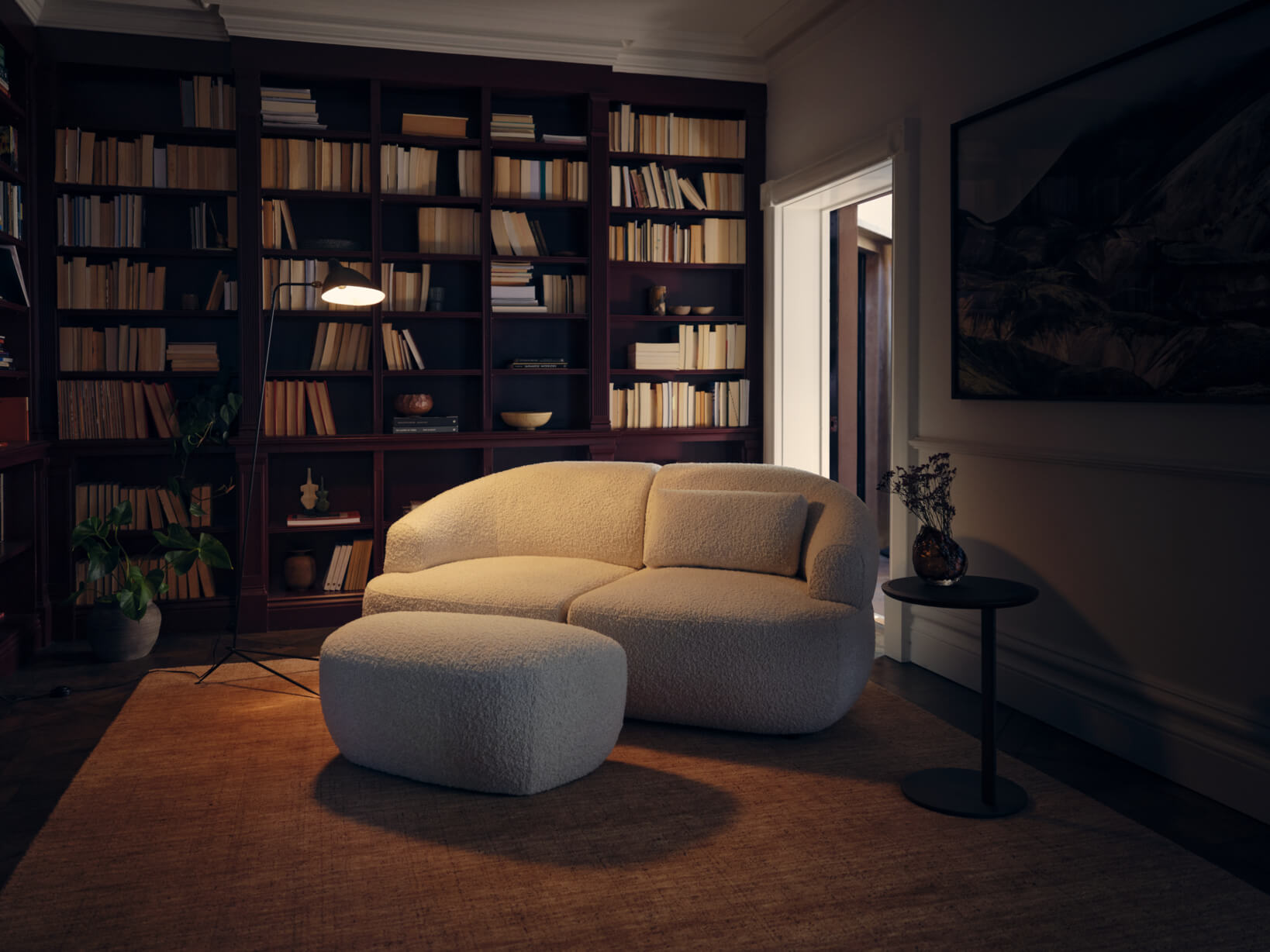 A curved, beige, bouclé sofa paired with a matching ottoman in a warm-toned home library with bookshelves and ambient lighting.