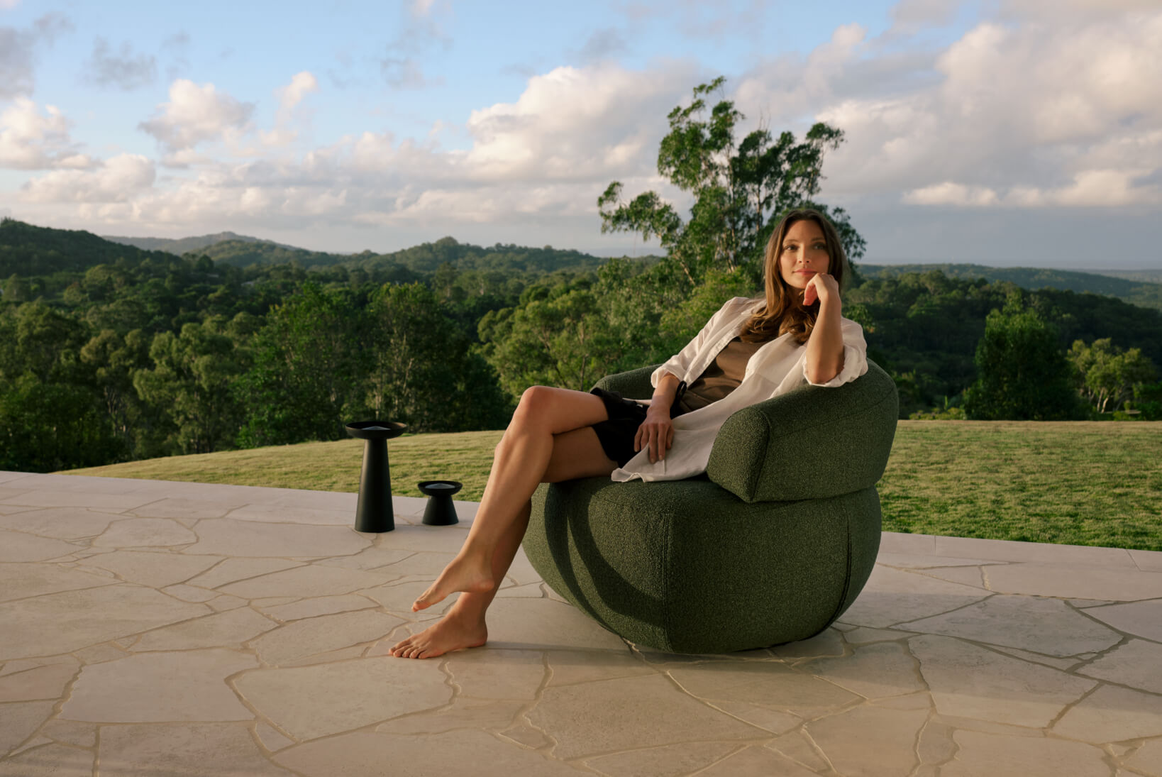 A woman lounging in a green, outdoor armchair, a perfect outdoor chair for reading, styled in a contemporary outdoor garden setting.