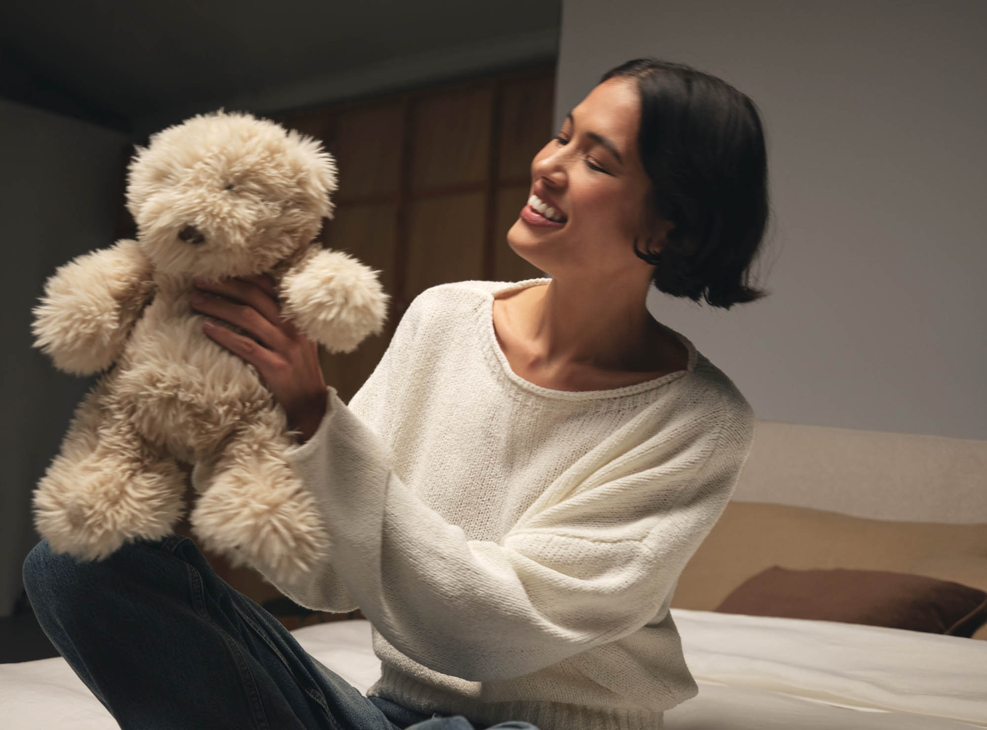 Woman smiling on the Evo retro bed holding up a cuddly teddy bear.