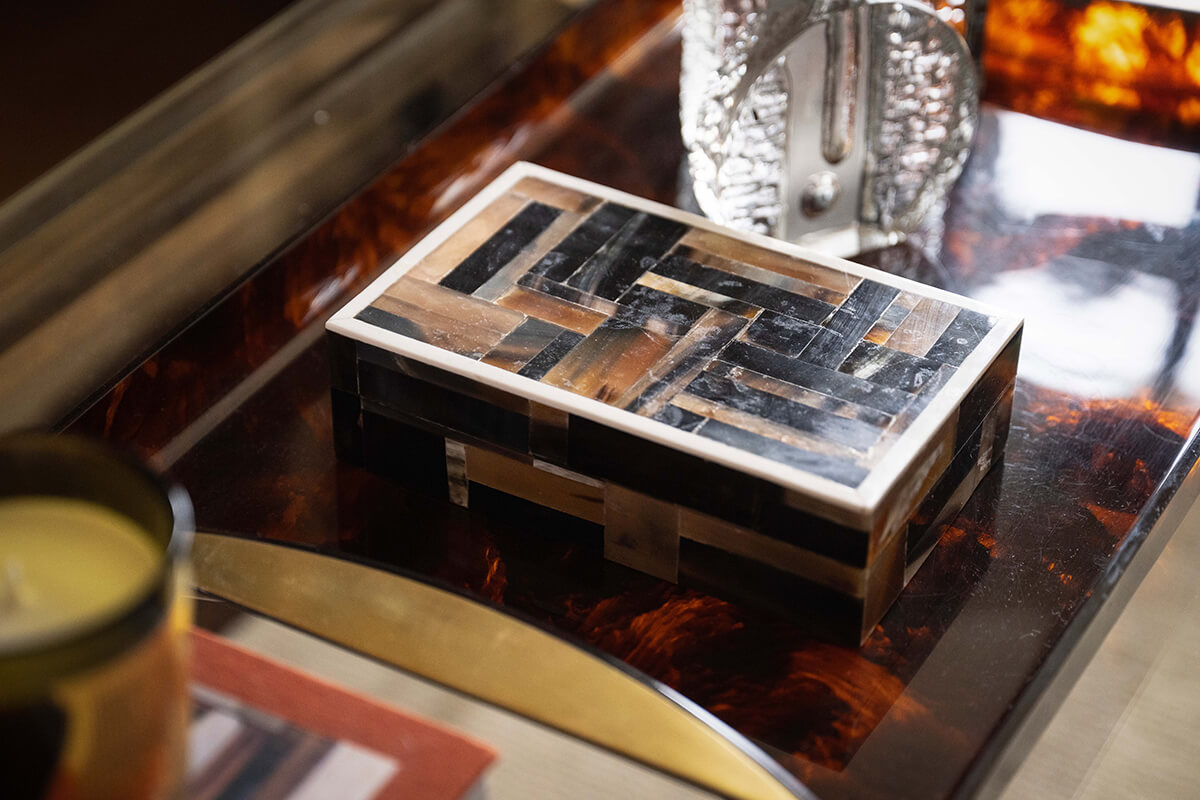 Sculptural copper wall art and walnut shelving styled with carved objects, books and collected ceramics.