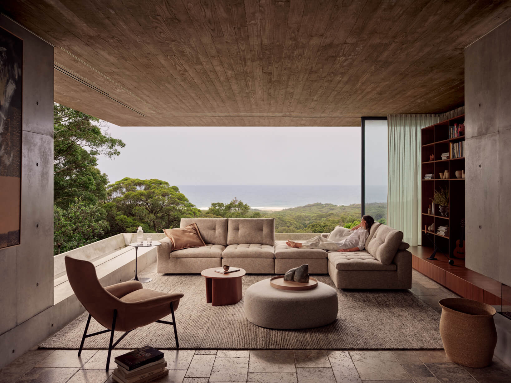 An L-shaped, modular sofa in a spacious living room, styled neutrally with open windowless walls and a coastal view.