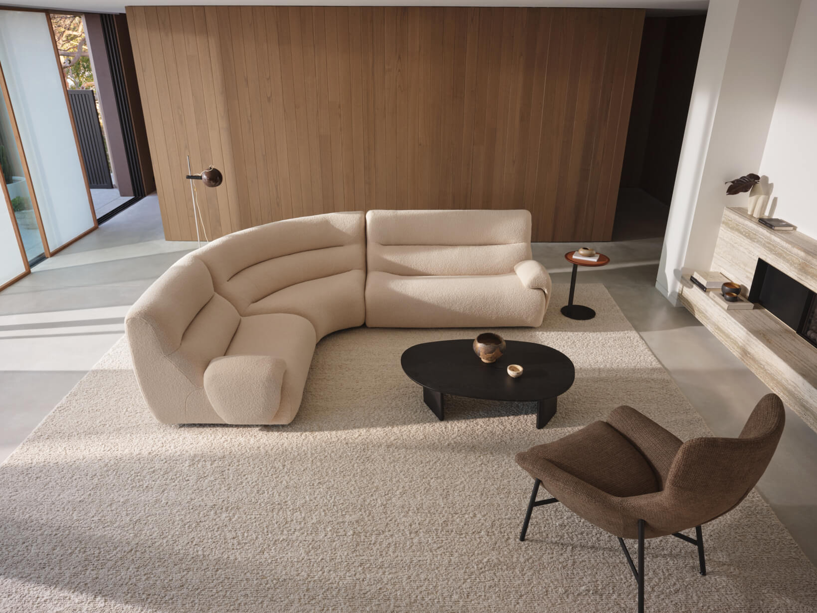 A high back modular sofa in a curve shape, finished in a neutral bouclé fabric in a contemporary tonal living room.