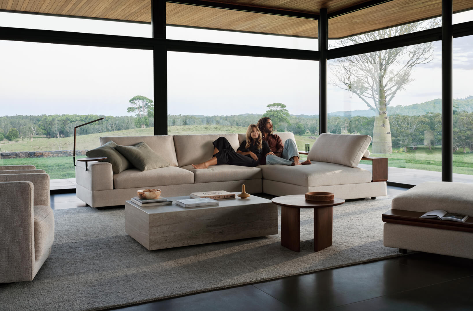 A couple lounge on a neutral, modular sofa in a light-filled contemporary living room with garden views.