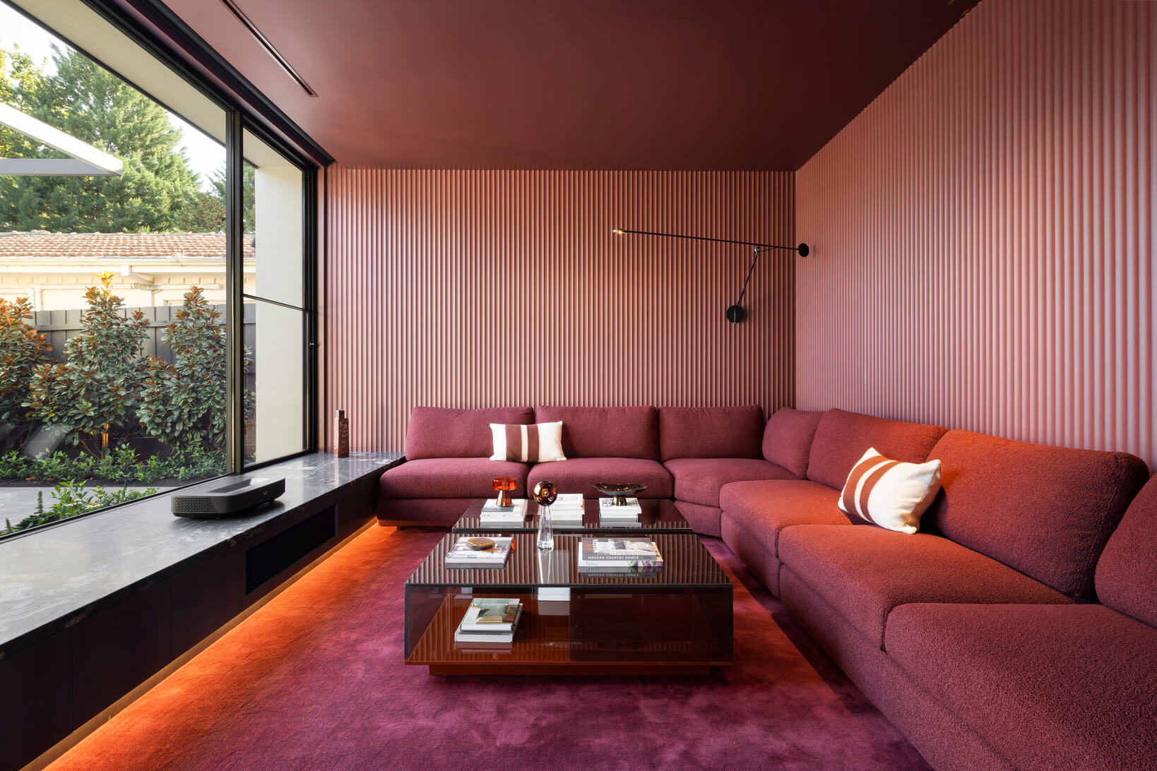 A sunken lounge designed as a games, cinema or entertainment room, colour drenched in deep burgundy tones from wall to sofa and floor.
