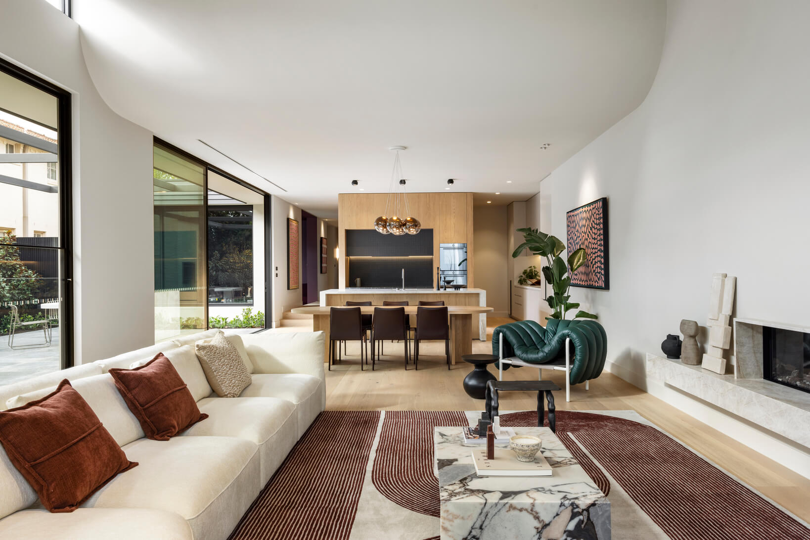 Open plan kitchen, living and dining space with a curved architectural ceiling and retro-inspired décor in warm brown tones.