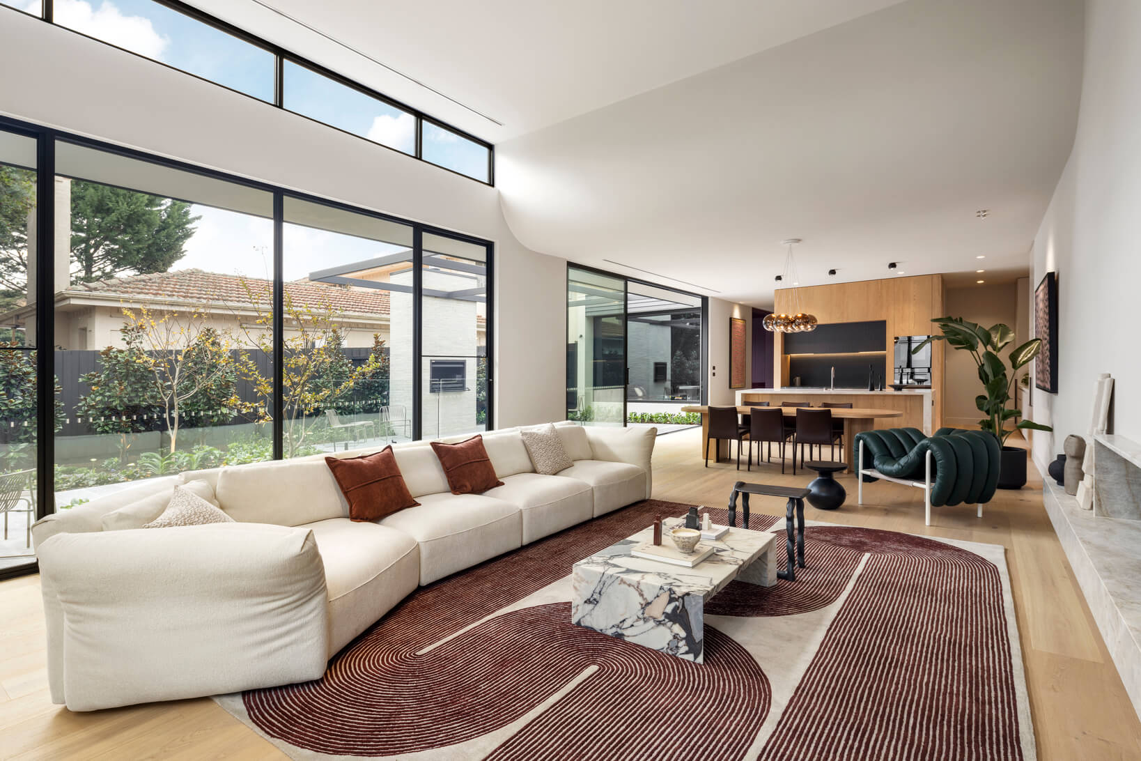 Large cream modular sofa with patterned rug anchors light-filled living space with floor-to-ceiling windows and garden outlook.