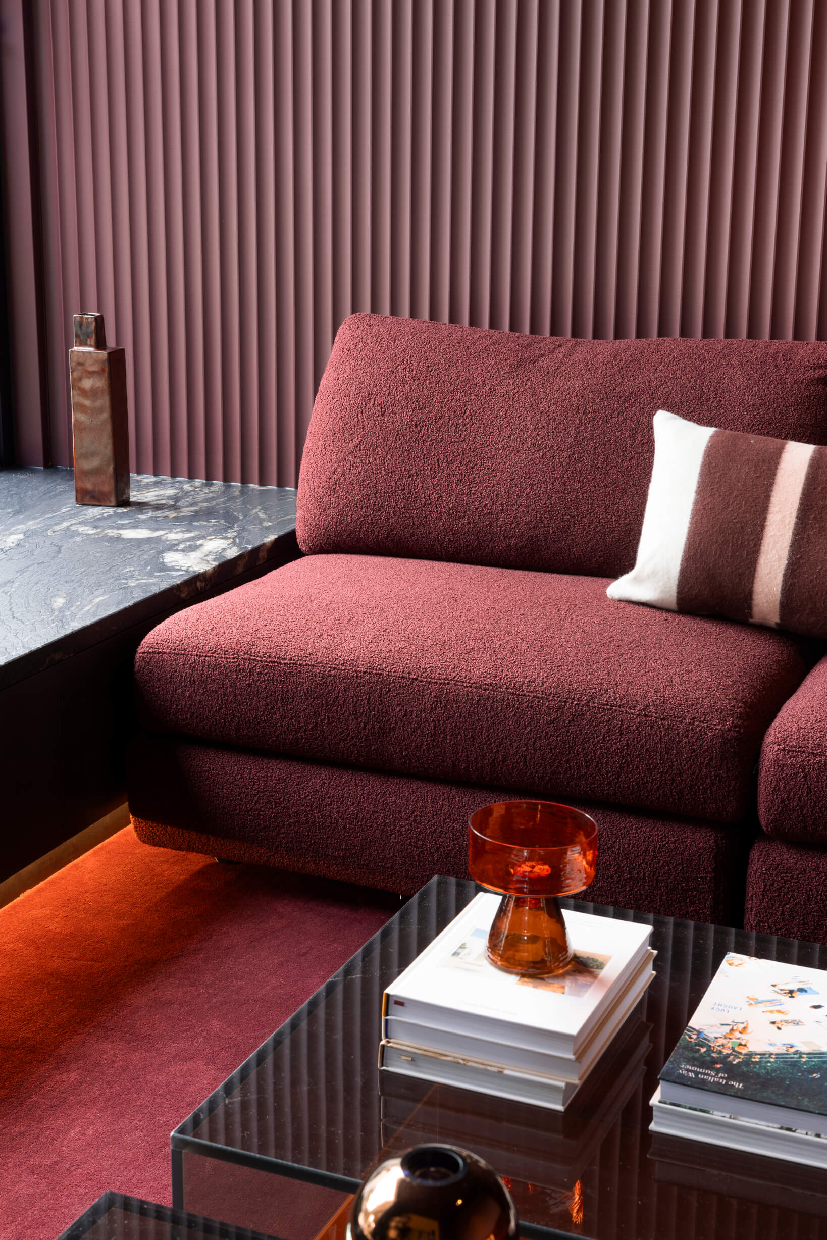 Modular sofa in a red wine bouclé fabric, complemented by burnt amber glassware and elegant black marble finishes.