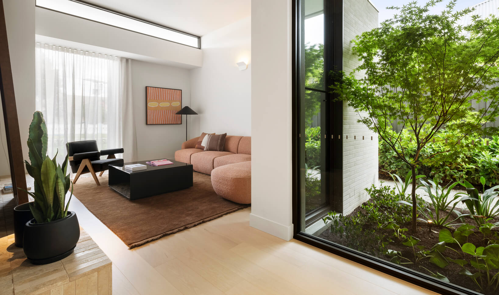Warm toned pink curved sofa with large rug creates a cosy, intimate reading nook in expansive open-plan home.
