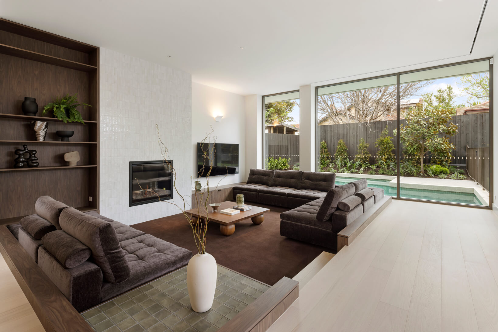 A cosy living room colour palette of chocolate and mocha mousse define a sunken lounge through rug, sofa, timber shelving and coffee table.