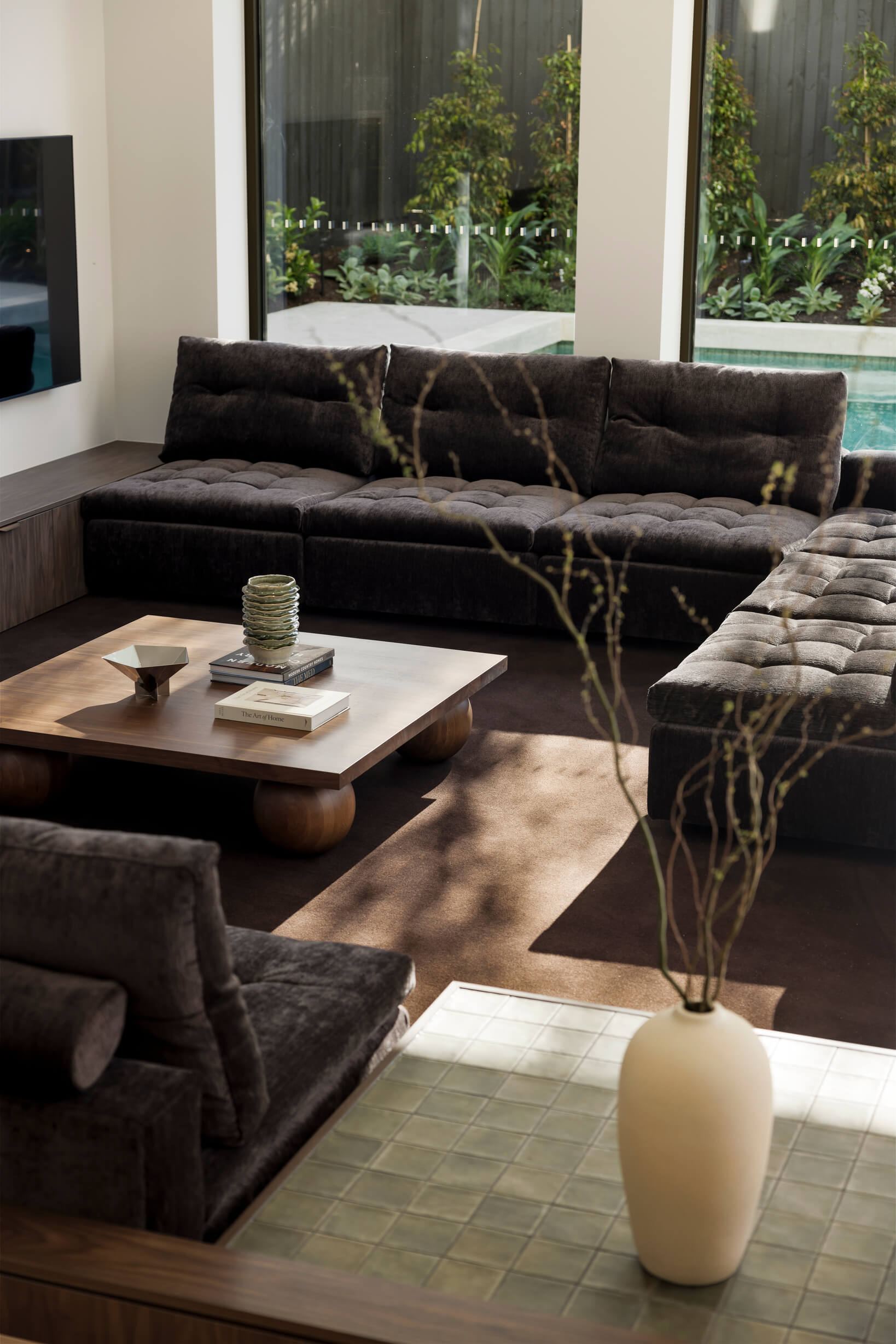 Light tiled side tables and ceramic décor styled in brown interior, creating indoor-outdoor flow with the view to pool outside.