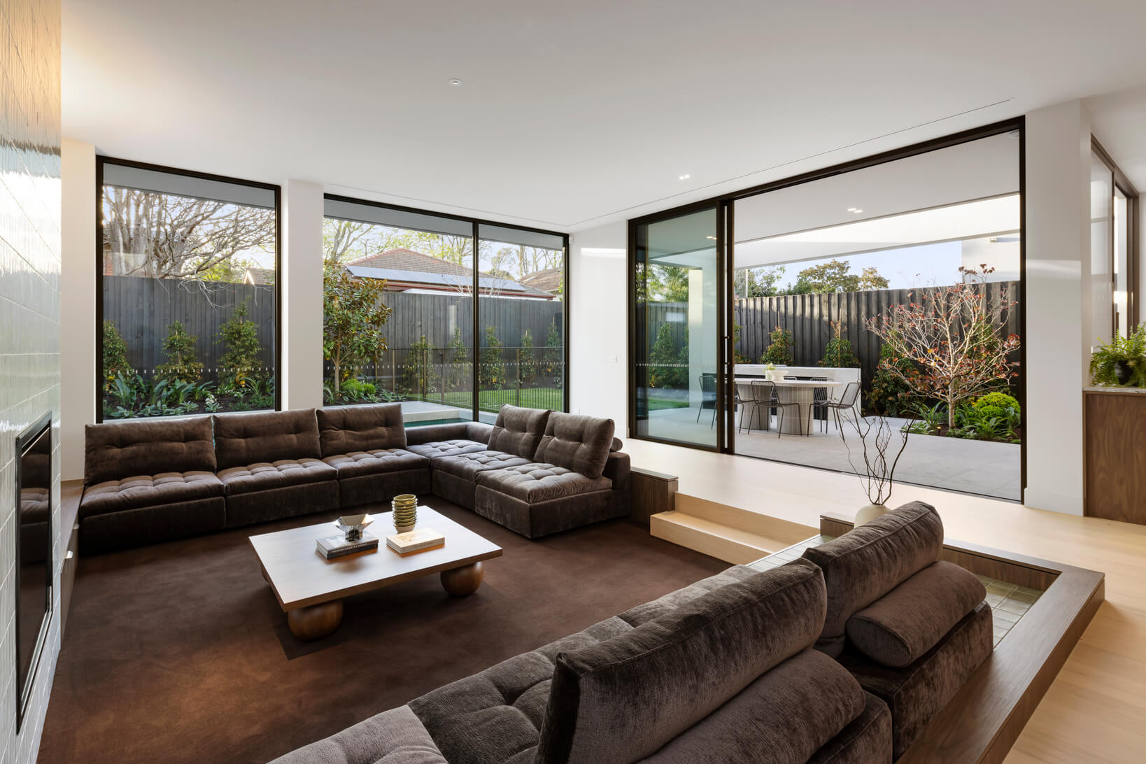 Modern living space with large floor to ceiling windows featuring a sunken lounge and brown velvet modular sofa.