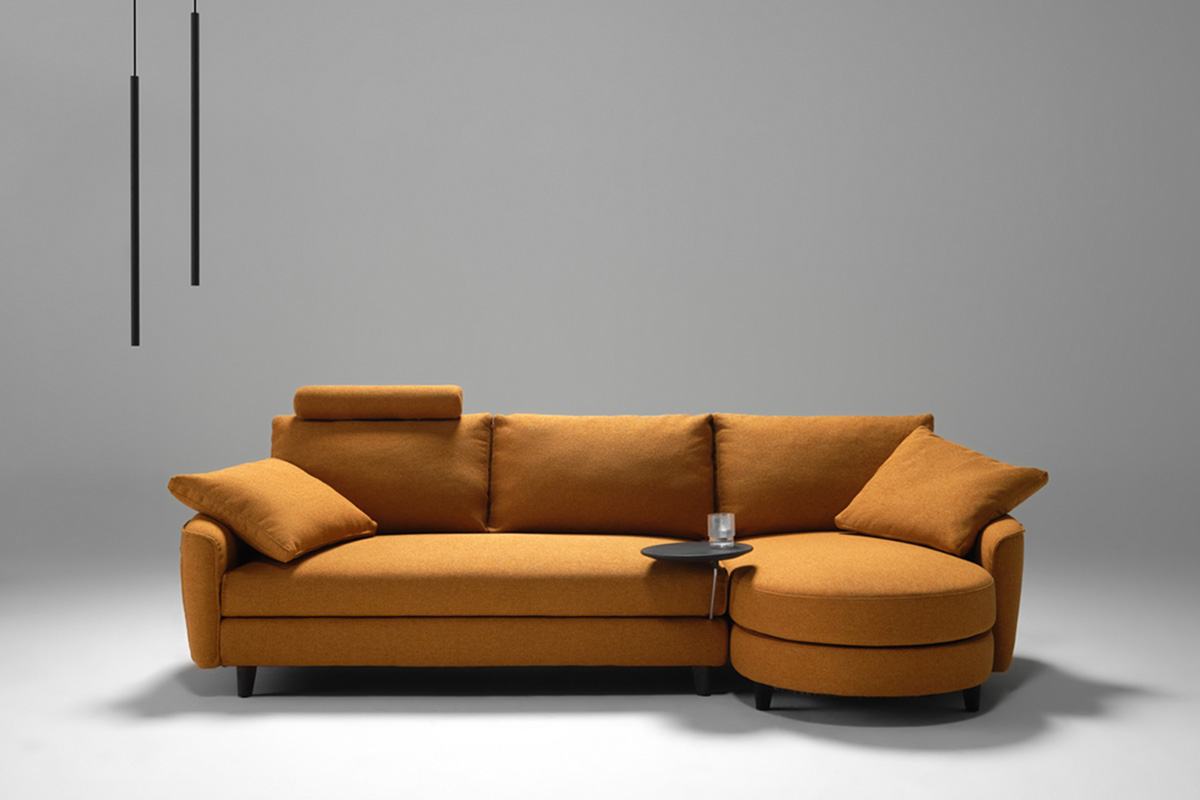 Curved modular sofa with chaise in ochre fabric, supportive headrest, and integrated timber charging table.