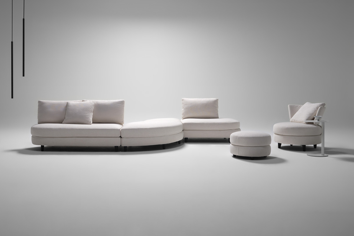 Large sectional sofa with curve modules in a minimalist studio setting, finished in a white fabric.