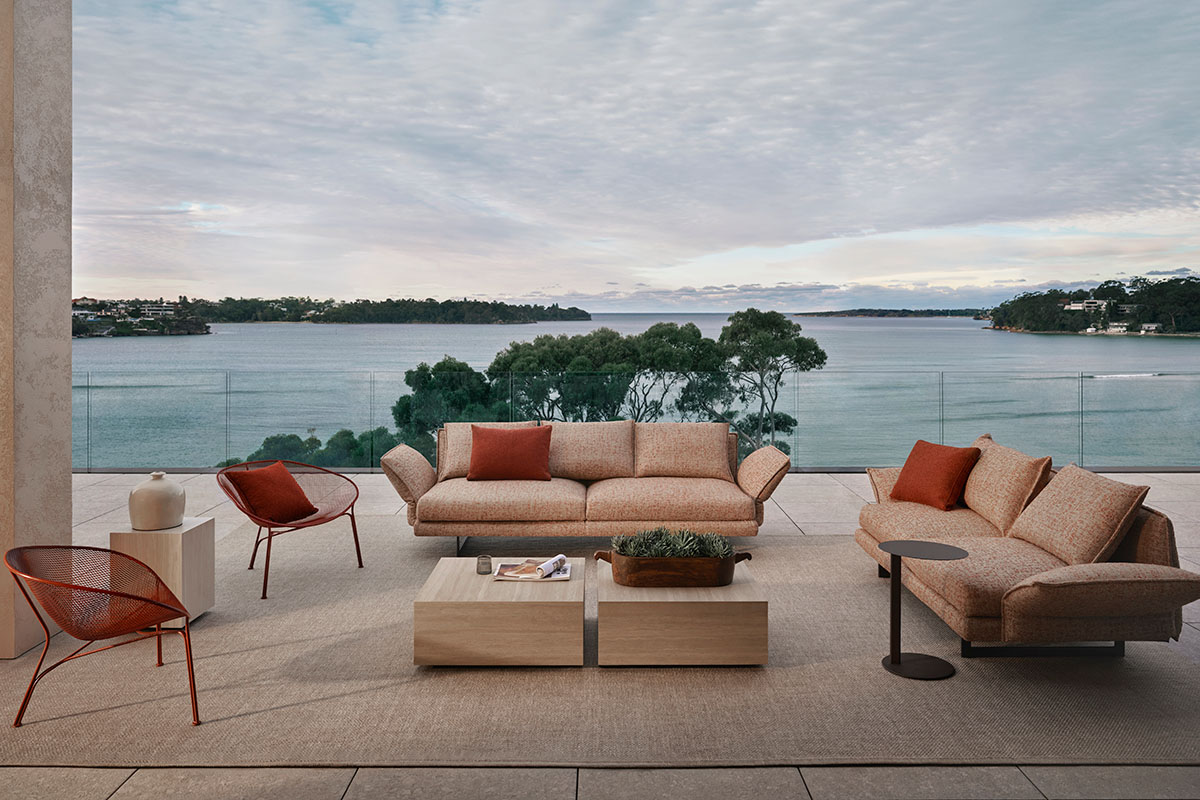 Soft blush outdoor furniture with russet accent chairs in a coastal outdoor lounge setting on a balcony overlooking the water.