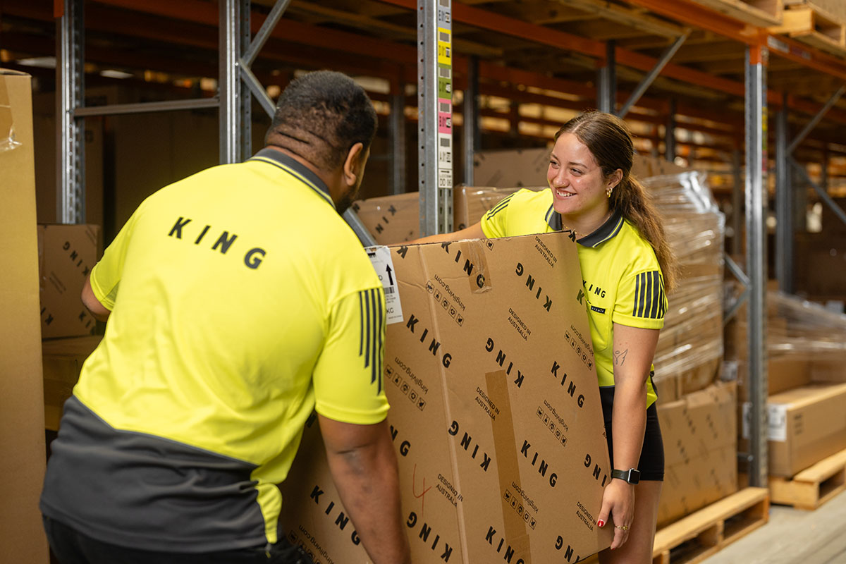 King Living employees in a warehouse smiling and lifting boxes.