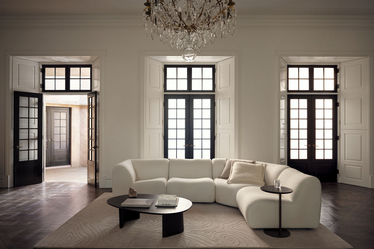 Floor to ceiling windows and doors with grand chandelier in open living space styled minimally with curved white modular sofa.