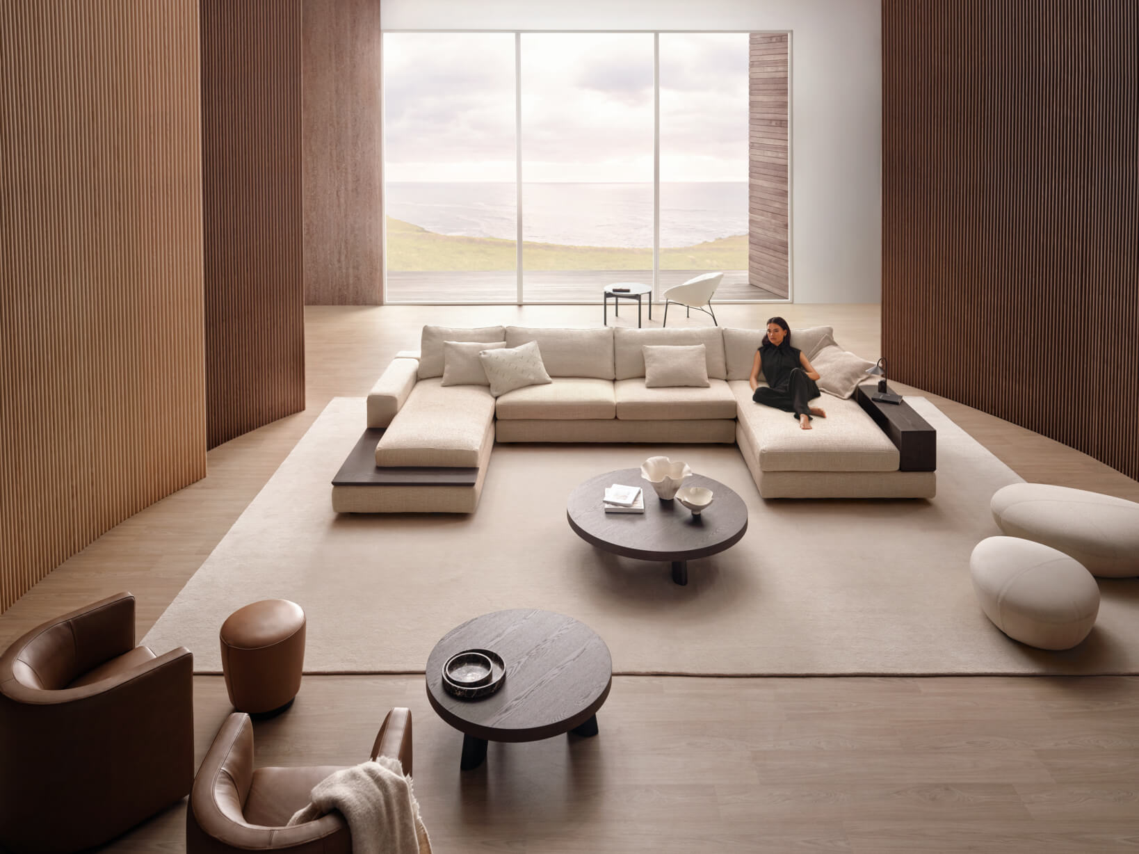 Modern spacious living room styled in light neutrals with timber panelling, a large rug, a modular sofa and leather occasional chairs.