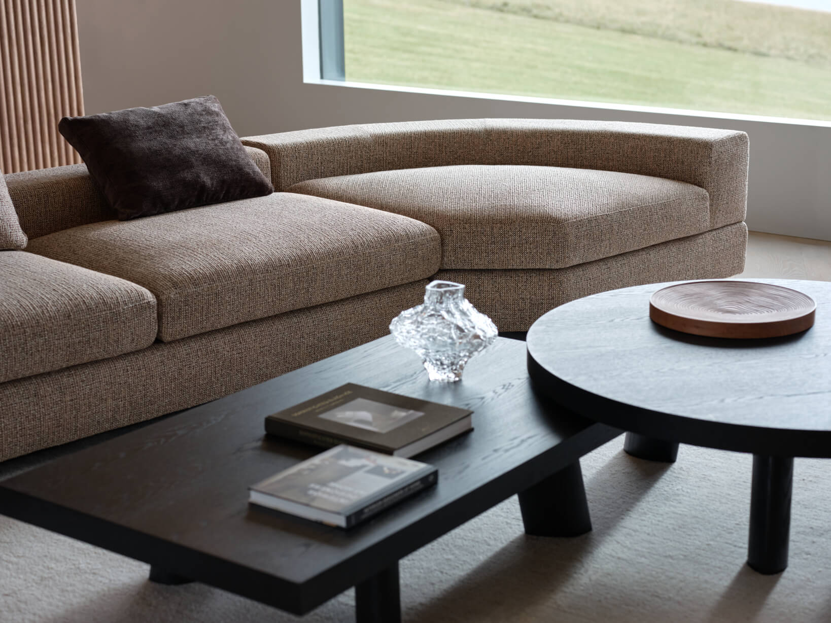 Curved modular sofa in earthy neutral fabric styled in a contemporary living space with timber accents.