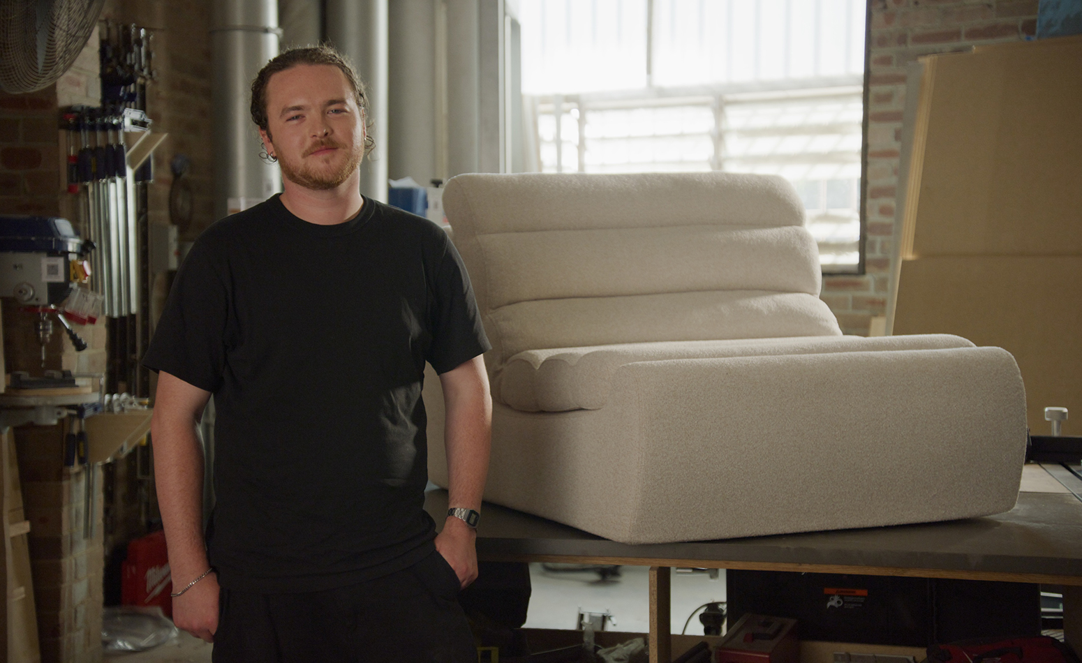 Designer stands in workshop beside a module of his sofa.