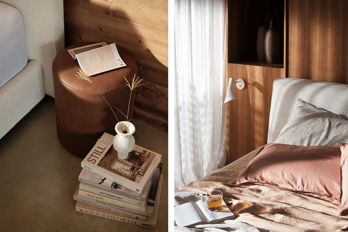 Layered bedding with blush cushions, ceramic styling, warm leather ottoman, stacked books create a relaxed, tactile setting.