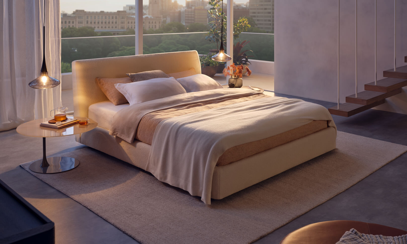 Softly lit bedroom overlooking city at dusk: storage bed, side table, tonal rug, twin pendant lights casting a gentle glow.