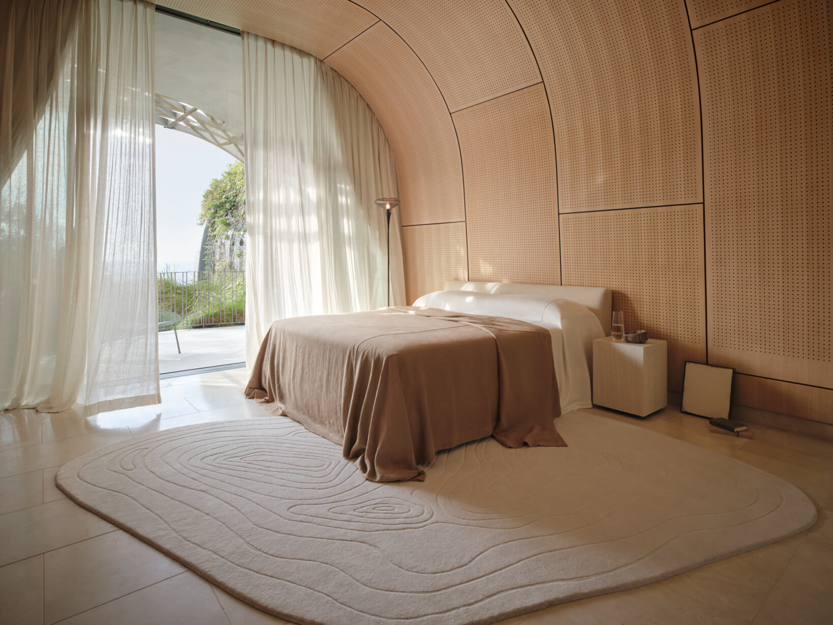 Neutral master bed, timber side tables, sculptural decor, organic shaped rug in a curved-panelled room.