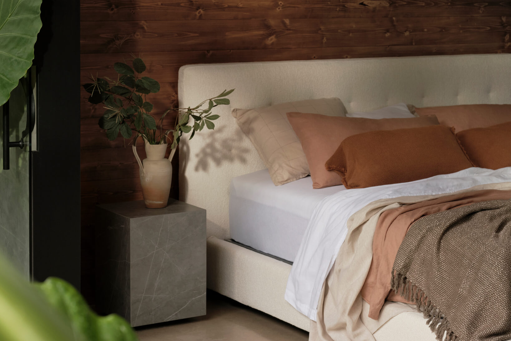 A curved neutral, king size bed is styled with tonal bedding in soft clay, blush and rust, creating a warm, earthy palette.