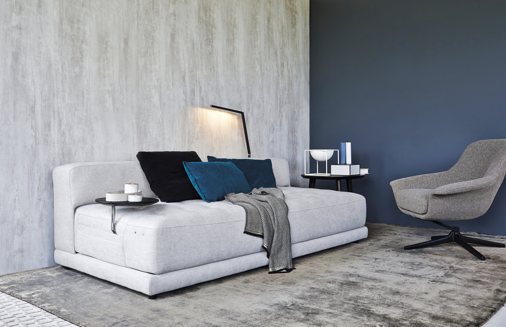 A light grey sofa bed with three cushions and a throw blanket.