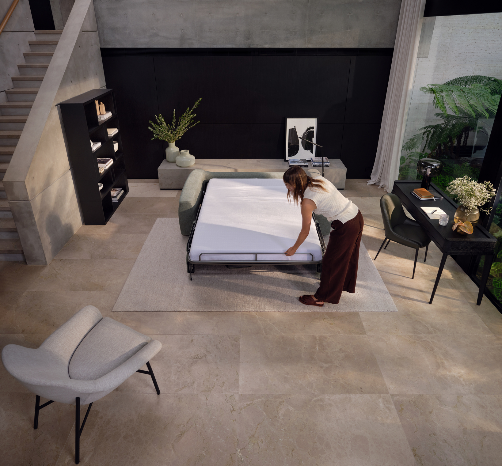 A woman setting up an open sofa bed in a modern living space.