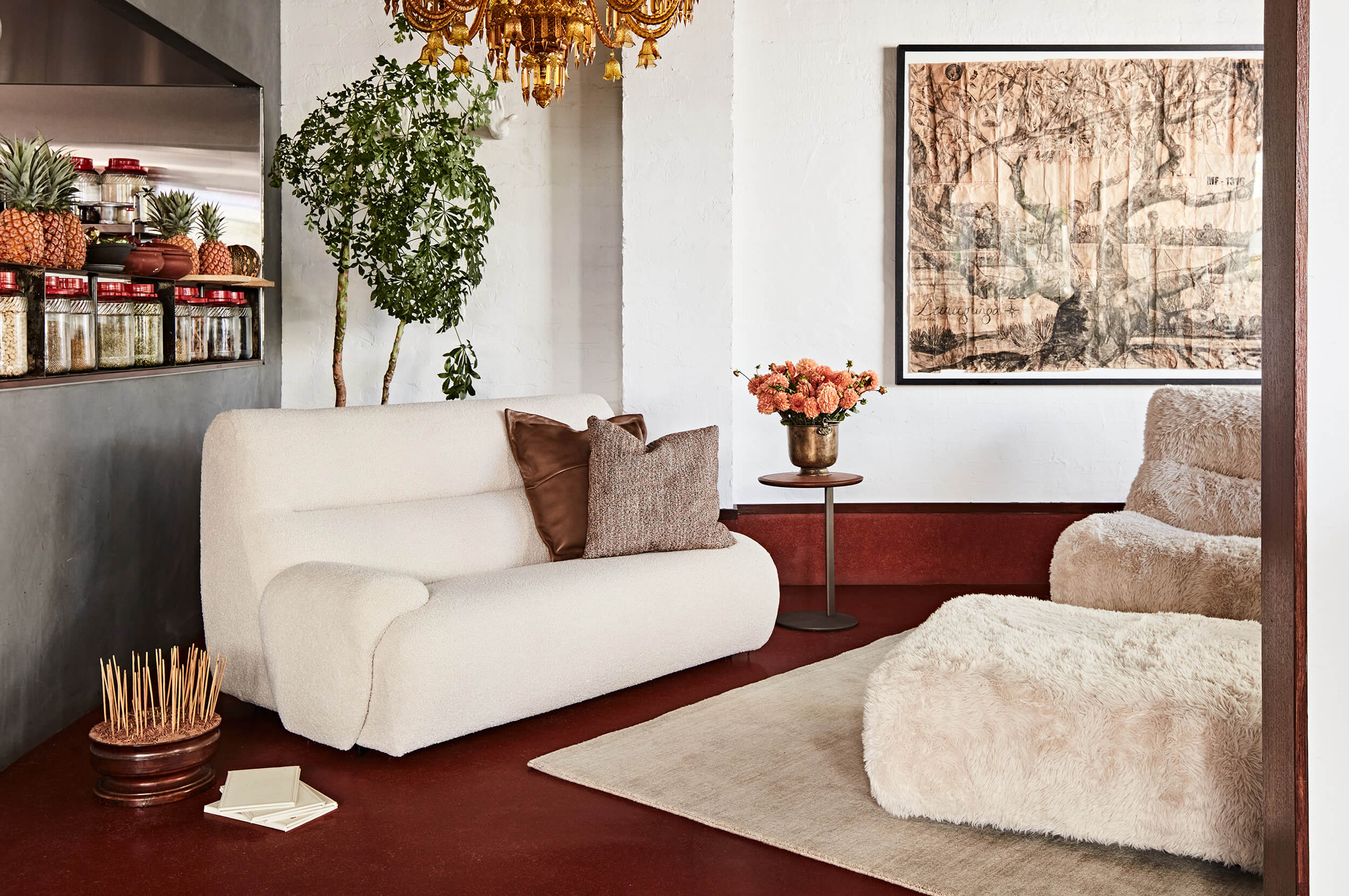 A modern eclectic living space with two neutral-toned sofas anchored by a bold, red-stained floor. Styled with layered textural accents and nature-infused decor.