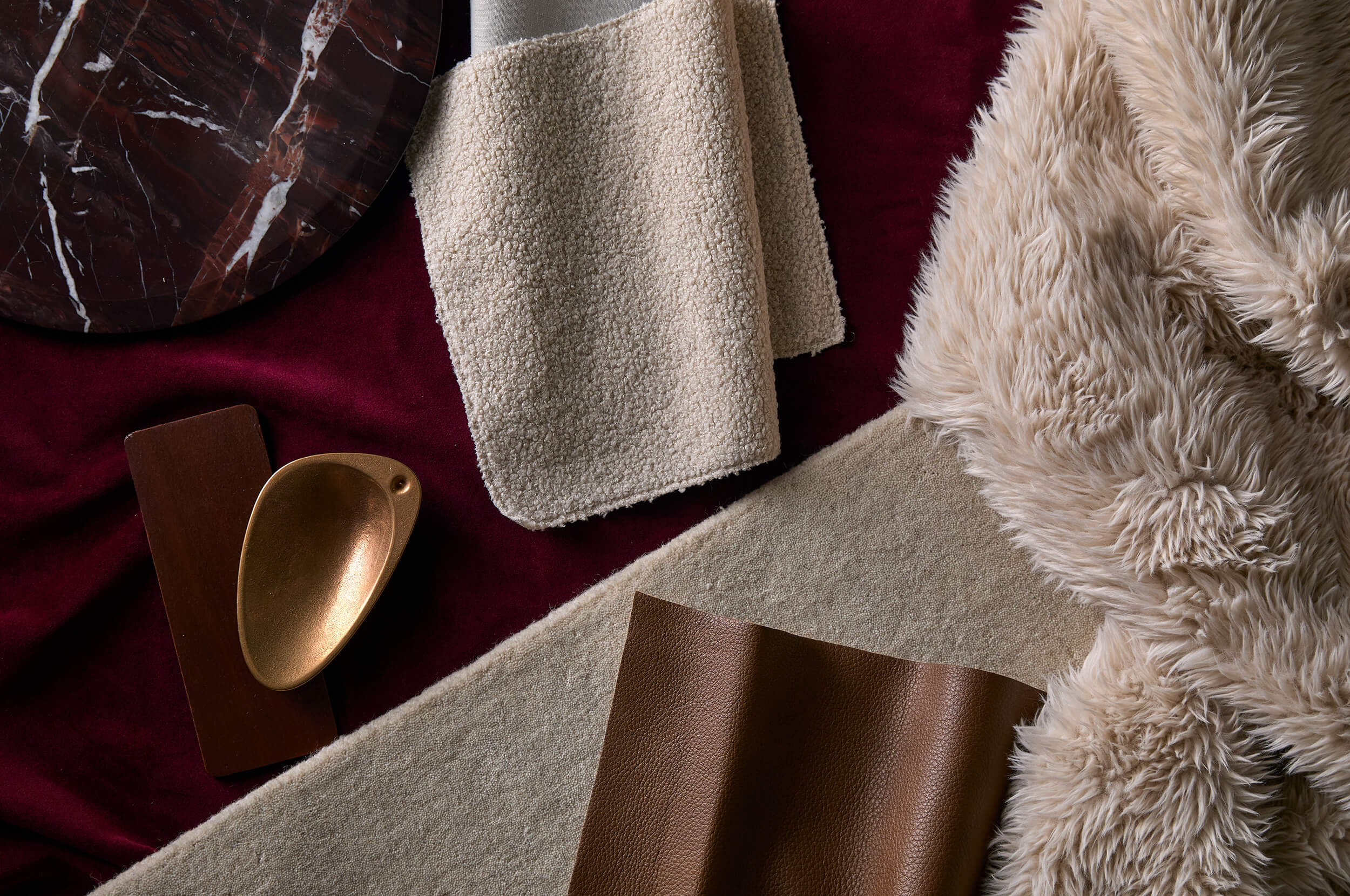 A flat lay of layered textures: soft faux fur, velvet and bouclé balance warm-toned leather and brass decor.