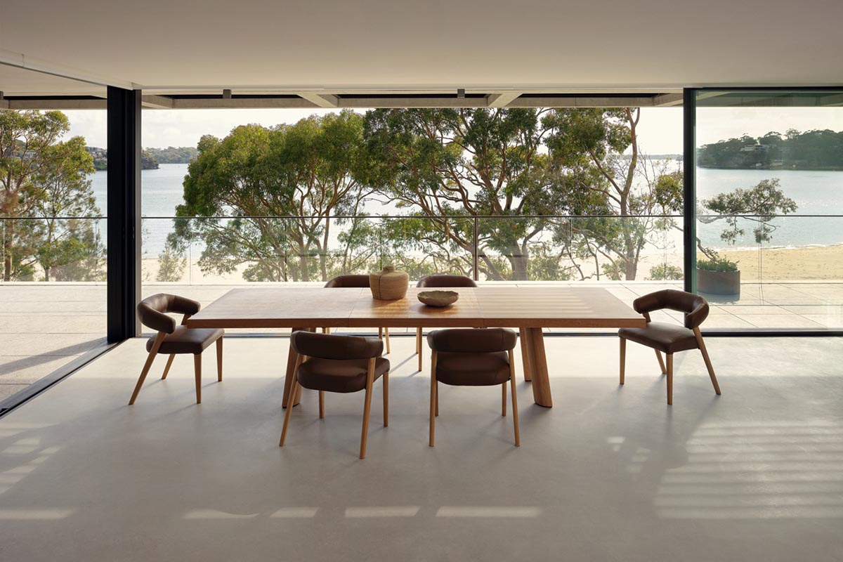 Minimalist open-plan dining room overlooking ocean views, styled with light timber dining furniture featuring an extension table.