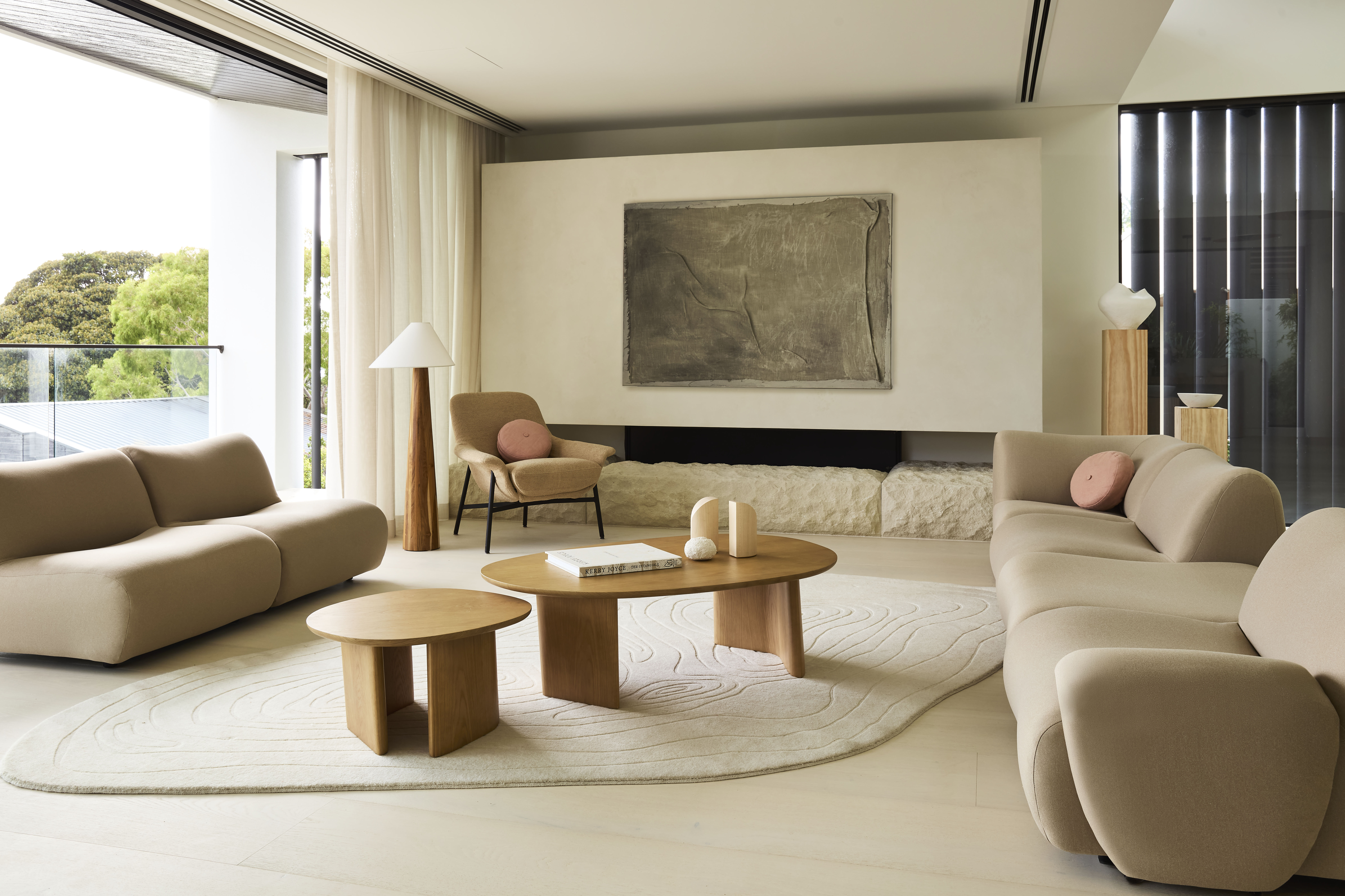 A modern living room with curved sofas and timber coffee tables, styled with a rug.