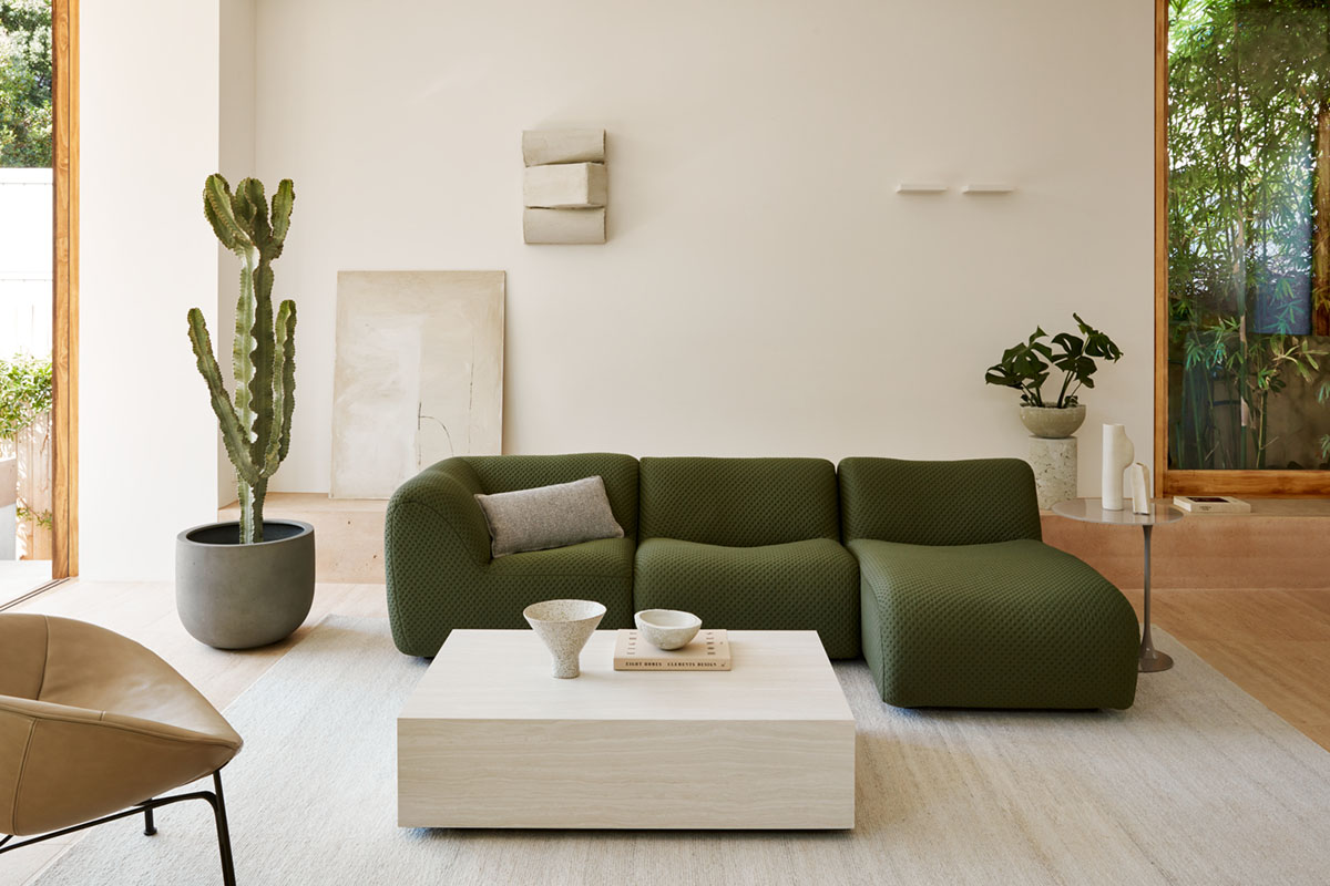 A contemporary apartment home styled with curved modular sofa and chaise in deep green bouclé.