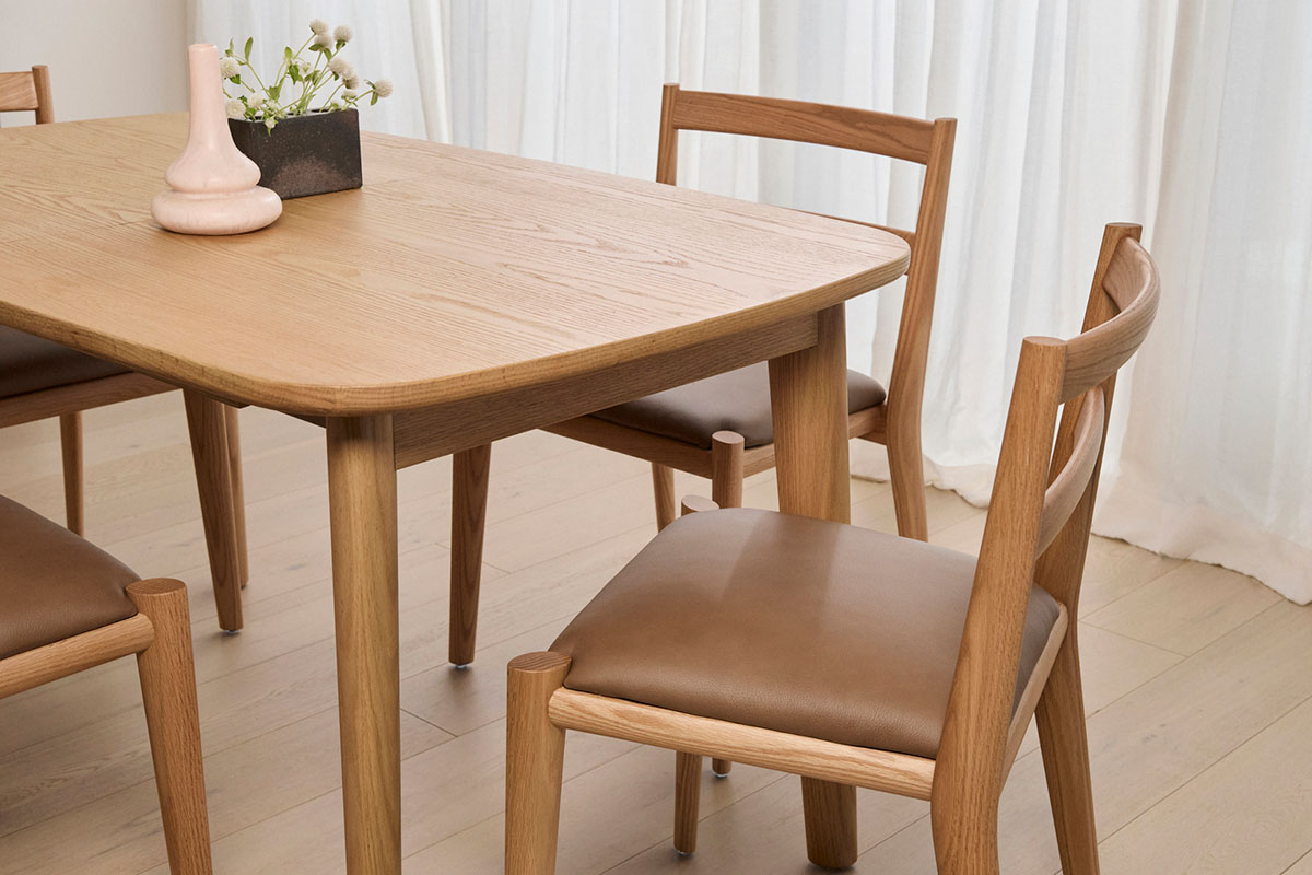 An open plan kitchen dining space with light timber dining furniture styled minimally with fresh florals.