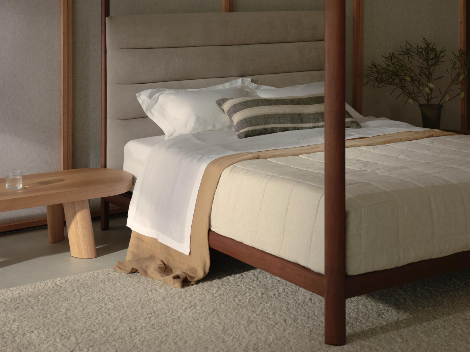 Timber four poster bed styled neutrally with a plush mattress and linen bedding.