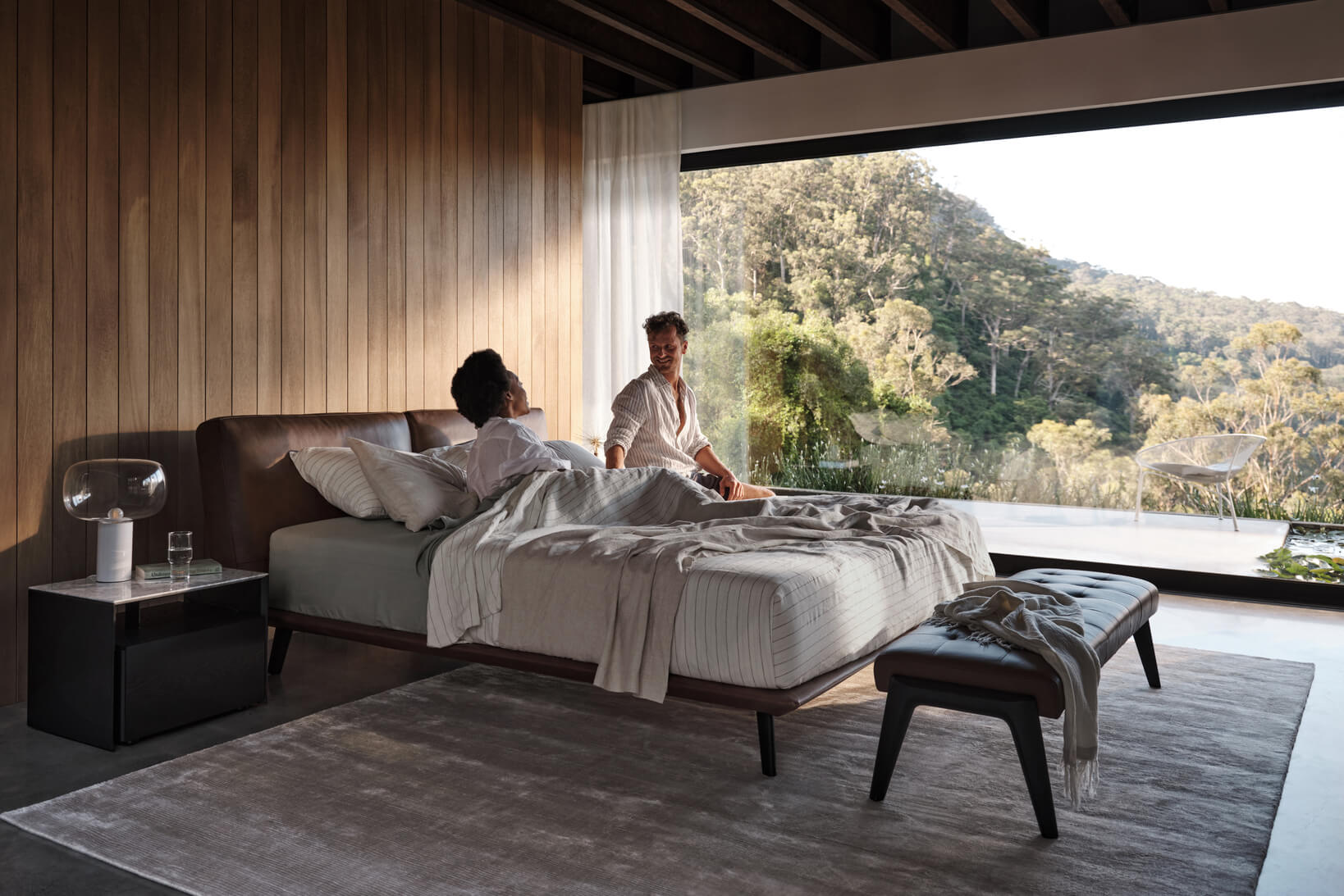 Couple with different sleeping positions lounge in bed in a contemporary bedroom.