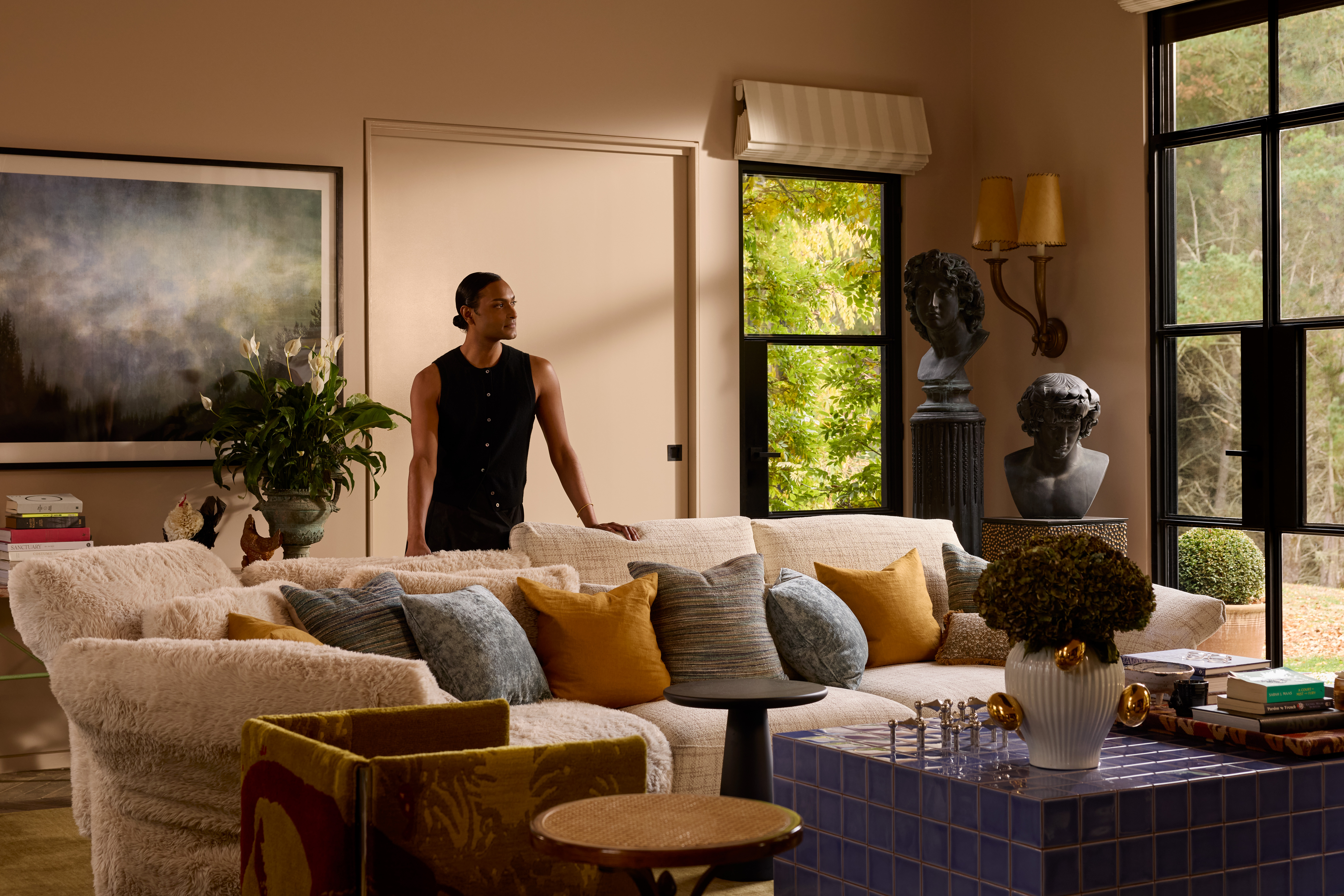 Interior designer Brahman Perera stands behind a modular sofa, styled in soft neutral fabrics in an eclectic living room.