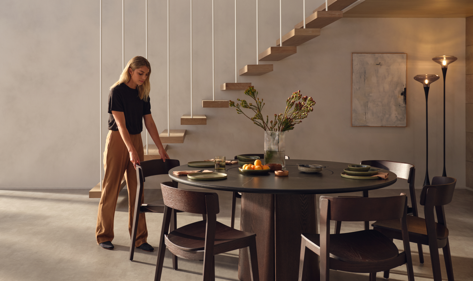 Woman measures her timber dining chairs around a round timber dining table in a modern small space.