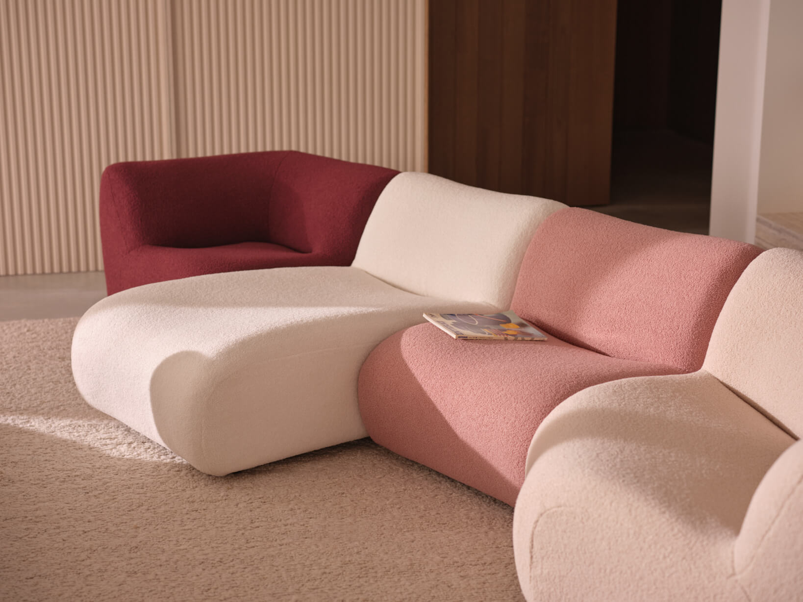 A curved, modular sofa with each module showcased in a different fabric colour, ranging from a deep maroon and soft blush to two neutral tones.