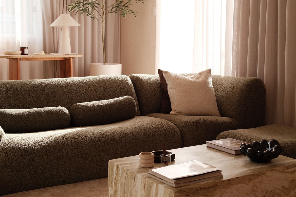 Curved low-profile modular sofa styling in a warm neutral living room with sheer curtains and a stone coffee table.
