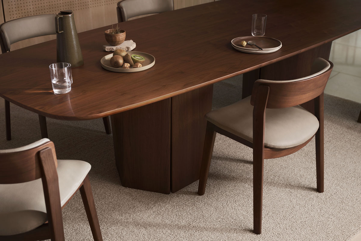 Oval dining table in warm walnut timber styled with contemporary timber and leather dining chairs.