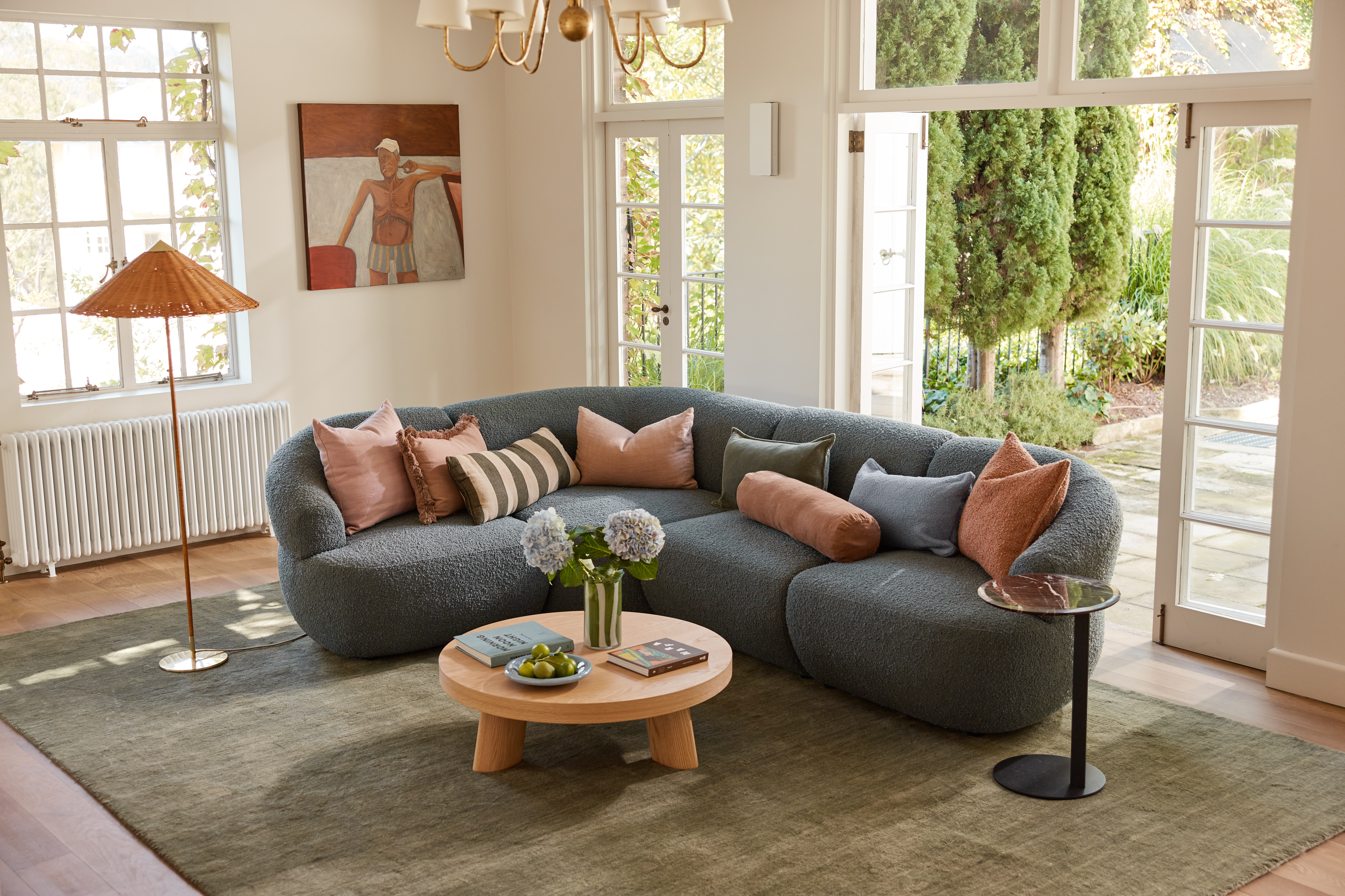A warm, sunlit living space styled with a teal bouclé modular sofa, complemented by earthy accents. Designer’s own cushions. Wall artwork by Dan Rushford.