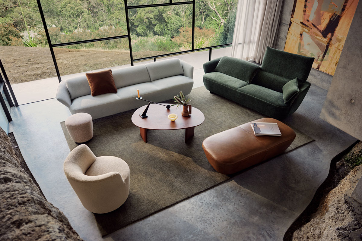 Nature-inspired living space with earthy green hues, soft-toned seating and sculptural coffee table framed by bushland views.