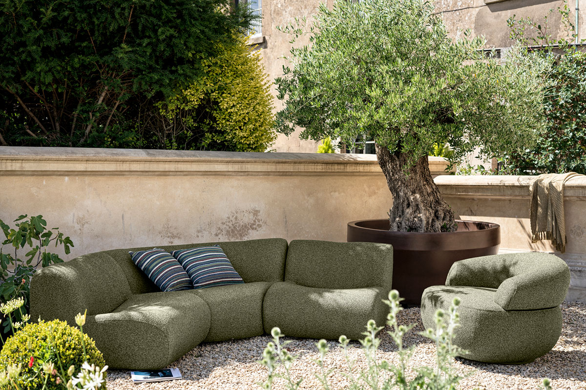 Durable outdoor bouclé fabric in olive green styled on modular outdoor sofa and plush swivel chair.