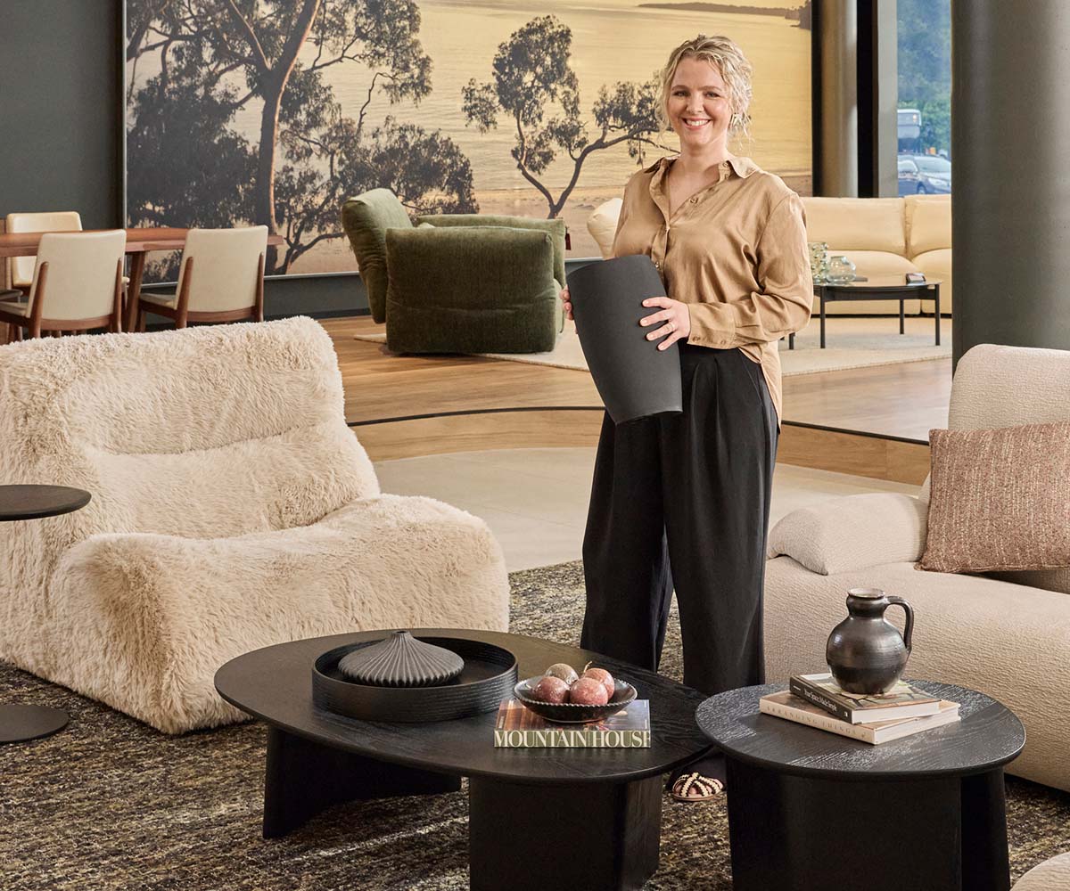Interior stylist Lucy Gough stands in the King Living Balgowlah Showroom showcasing how to style a black coffee table.