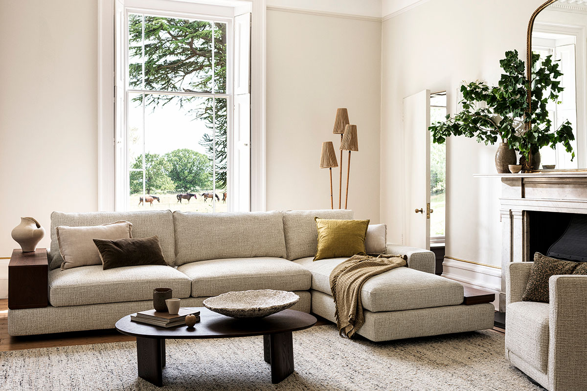 Large L Shaped neutral sofa in a living room with neutral walls, a fireplace and a wooden coffee table.