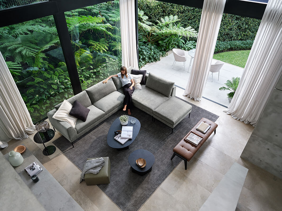L-shaped, modular sofa in sage green fabric styled with tonal cushions and black accent tables, set in a serene indoor-outdoor living space.