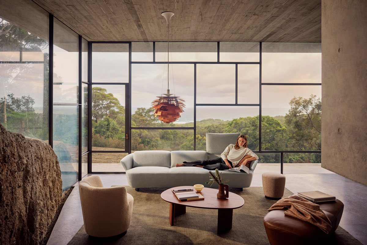 Living room with raw rock wall and floor-to-ceiling windows, styled with timber coffee tables, neutral sofa and views of greenery.